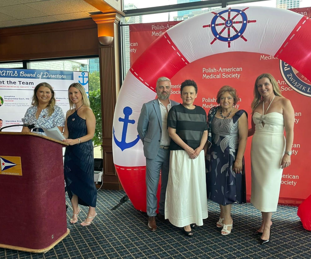 Polonijni lekarze z Chicago podczas „Żeglarskiej Nocy” w Chicago Yacht Club. Na zdjęciu widać dr Josephine Długopolską-Gach przy mównicy, obok niej stoją inne osoby, w tym mężczyzna i trzy kobiety. W tle czerwona ścianka z logo Polish-American Medical Society. Więcej o tym wydarzeniu znajdziesz na naszym portalu.