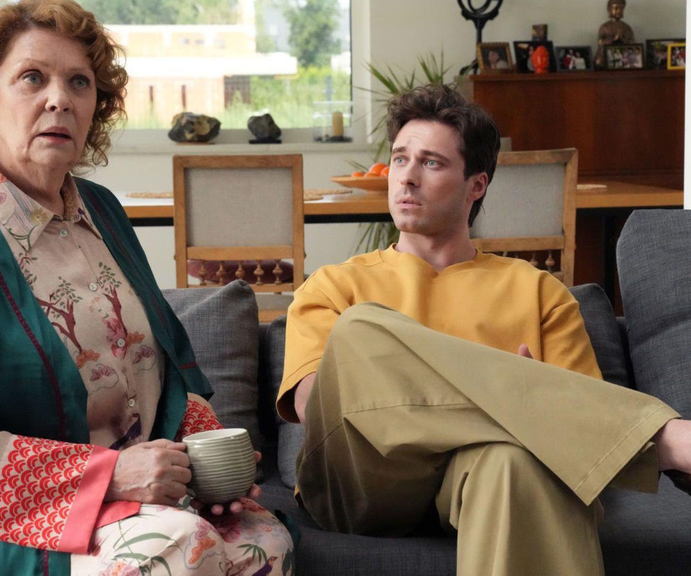 Józefina (Elżbieta Jarosik) z zatroskaną miną siedzi na kanapie obok Cezarego (Marcel Opaliński), który ma na sobie żółtą koszulkę i beżowe spodnie. Kobieta trzyma w ręku kubek, patrząc przed siebie. Obraz z serialu Barwy szczęścia można zobaczyć na Super Seriale.