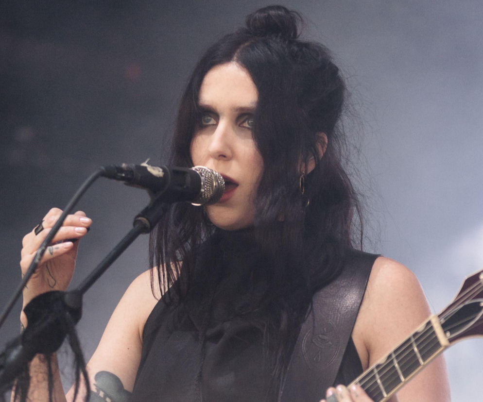 Chelsea Wolfe z gitarą śpiewa do mikrofonu podczas koncertu. O jej występie w Warszawie przeczytasz na EskaRock.