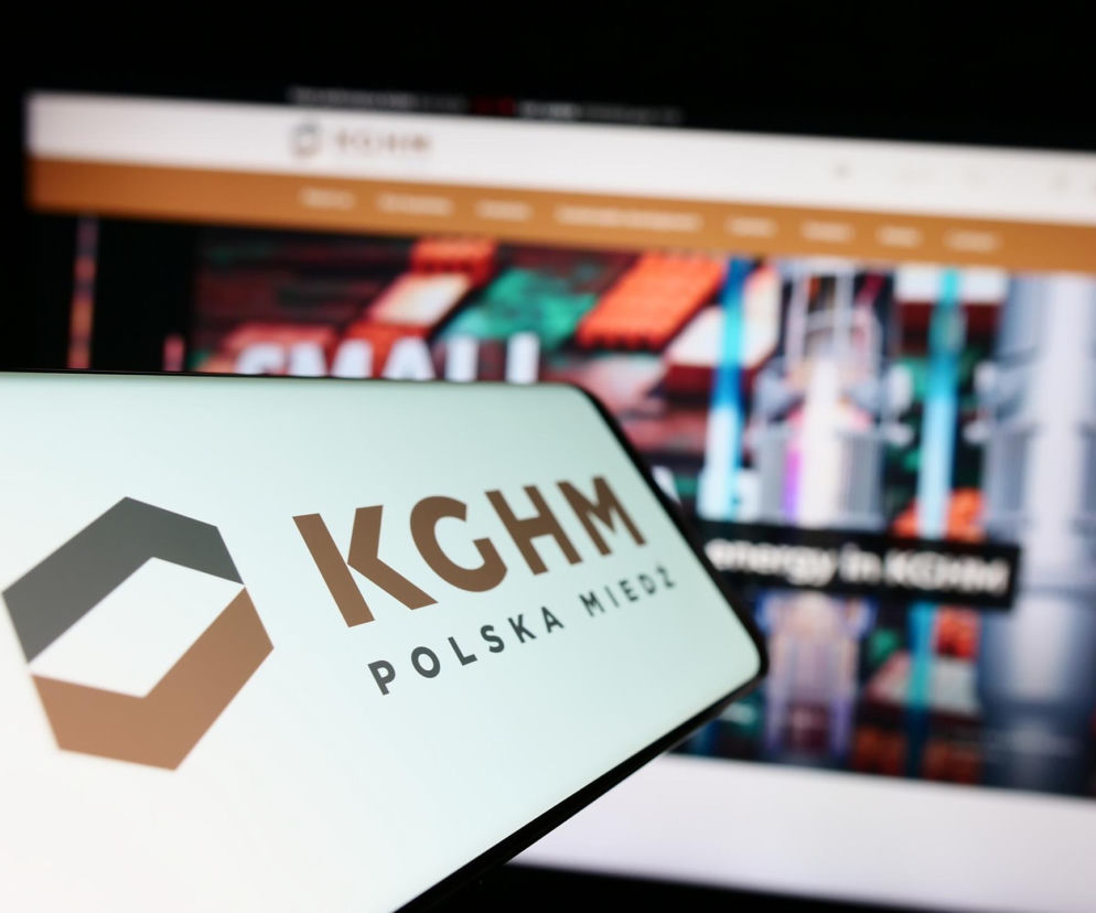 Logo KGHM Polska Miedź na ekranie smartfona, z niewyraźnym tłem strony internetowej KGHM na monitorze, ilustrujące poszukiwania nowego prezesa oraz wyzwania dla spółki, o czym można przeczytać na Super Biznes.