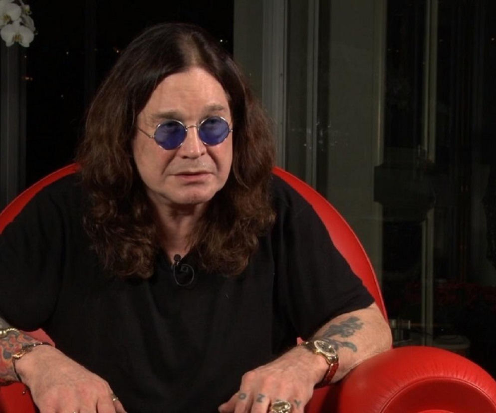 Muzyk Ozzy Osbourne w niebieskich okularach siedzi w czerwonym fotelu. O historii festiwalu Ozzfest przeczytasz w EskaRock.