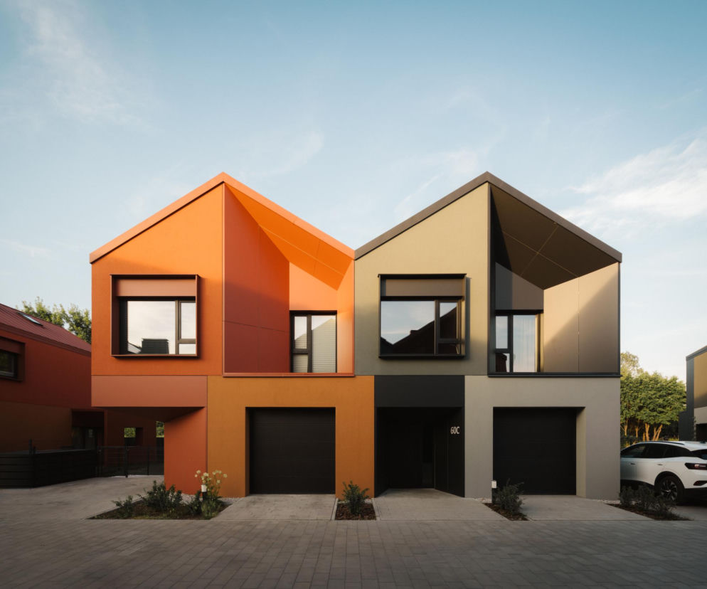 Dwa asymetryczne domy bliźniacze o pomarańczowej i szarej elewacji z wnękami. O architekturze przy Borków czytaj na Architektura.