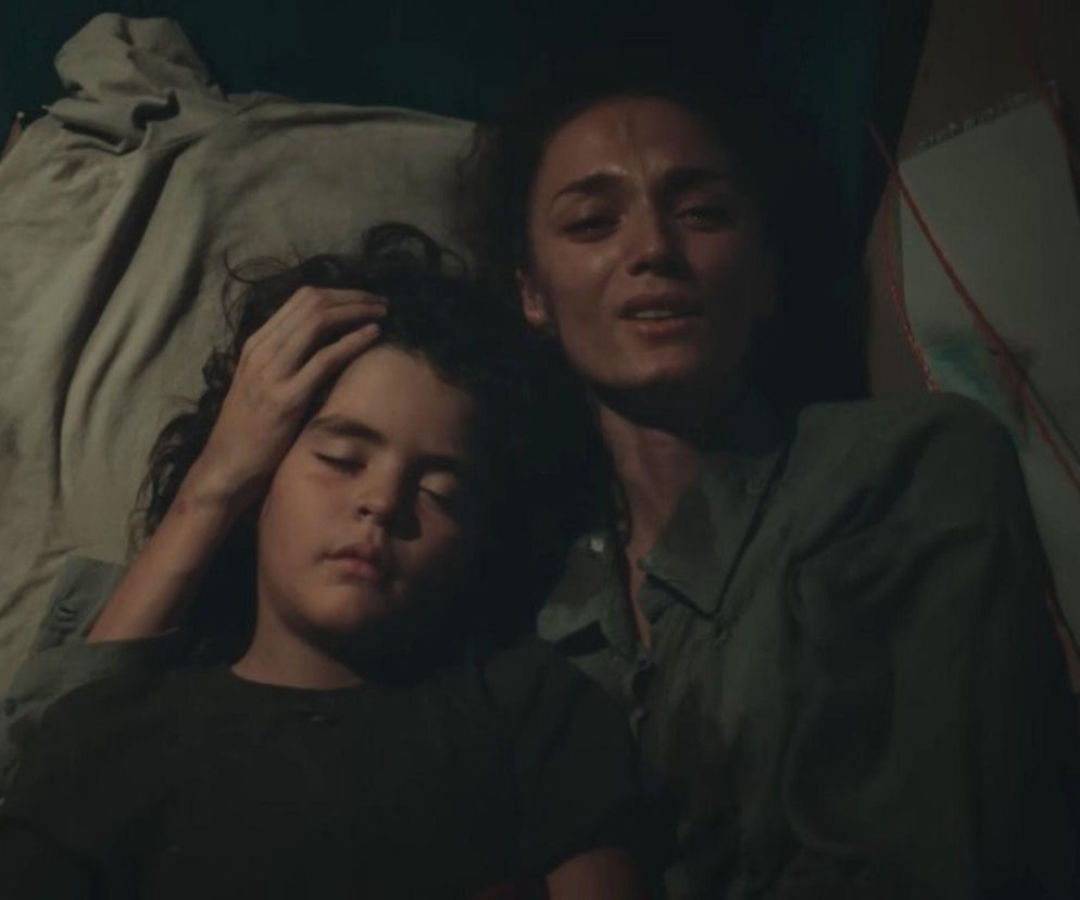 Kobieta o brązowych włosach, wyglądająca na zrozpaczoną, leży obok śpiącego dziecka, głaszcząc je po głowie. Oboje są w ciemnym, zaniedbanym miejscu. Scena z serialu „Dziedzictwo”, o którym można przeczytać na Super Seriale, ukazuje trudne losy Nany i Yusufa.