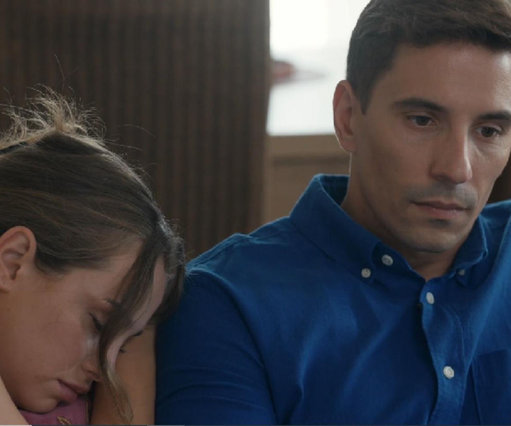 Aktorka Wiktoria Gąsiewska jako Oliwka śpiąca na ramieniu aktora Jakuba Sokołowskiego grającego Tomasza, który patrzy ze smutkiem w dół. Scena z serialu Barwy szczęścia o zmęczeniu Oliwki i jego konsekwencjach. Więcej informacji o serialu znajdziesz na Super Seriale.