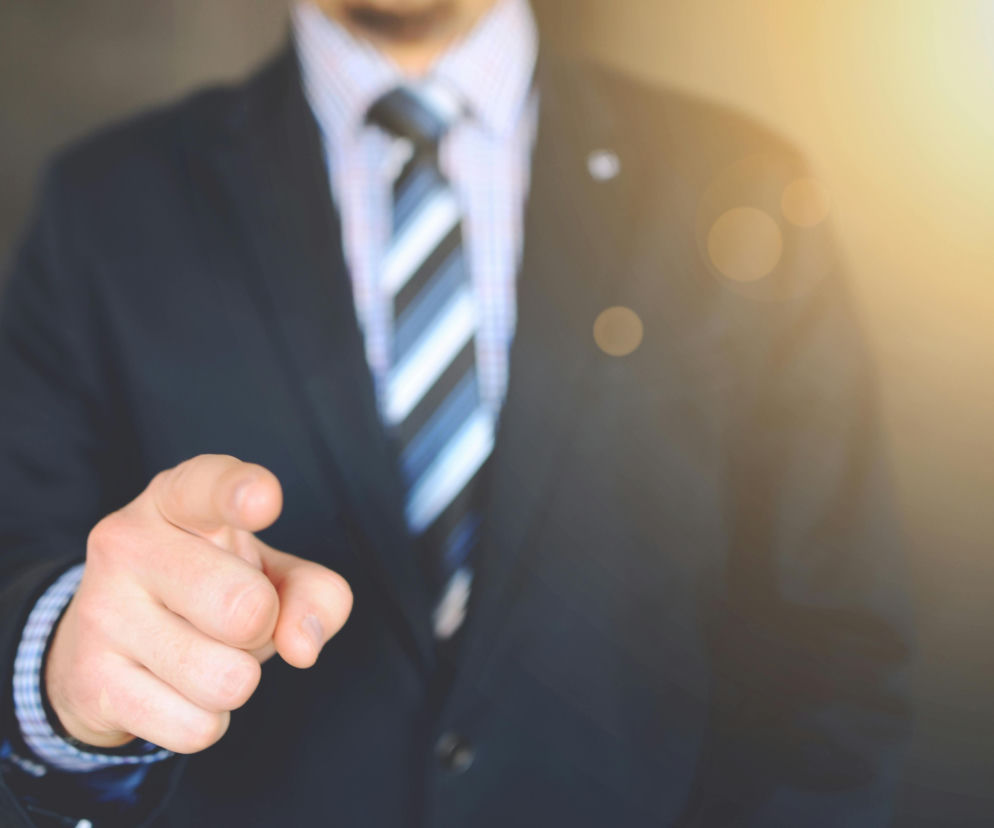 Mężczyzna w eleganckim garniturze i krawacie wskazuje palcem w stronę odbiorcy, symbolizując wybór nowych kierunków ekspansji zagranicznej polskich firm. Wskazuje to na dynamikę i nowe możliwości, o których możesz przeczytać na portalu Super Biznes.