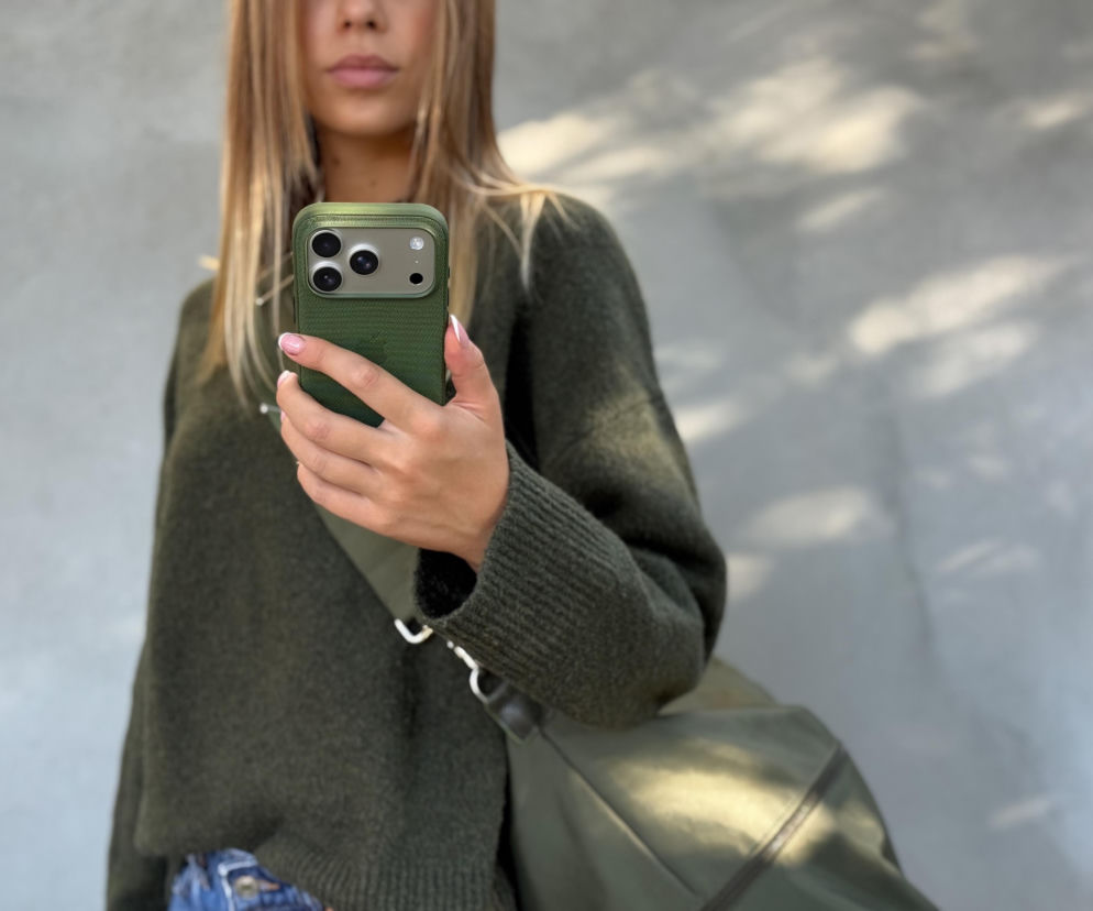 Dłoń kobiety trzymającej smartfon w zielonym etui z widocznymi aparatami. O nowym iPhone 18 przeczytasz w serwisie Eska.