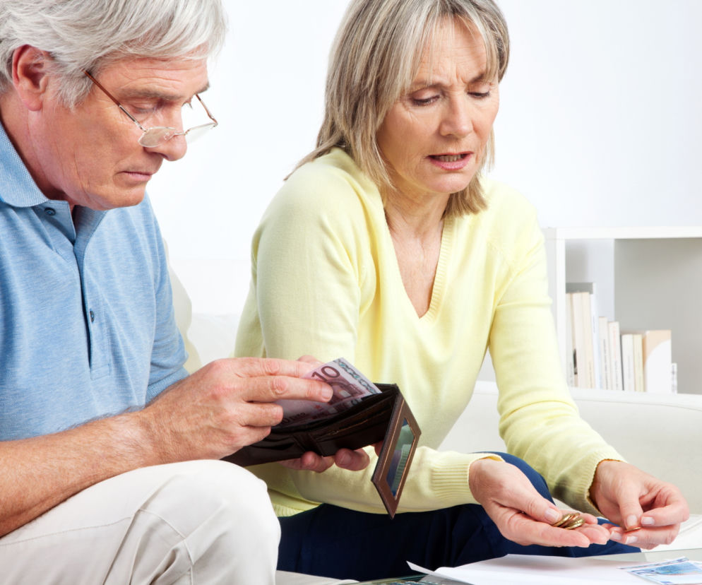 Para seniorów liczy pieniądze: mężczyzna wyjmuje banknot z portfela, kobieta trzyma monety, zmartwieni dodatkami do emerytur. O wsparciu finansowym dla emerytów, w tym Małżeństwo plus, przeczytasz na portalu Super Biznes.