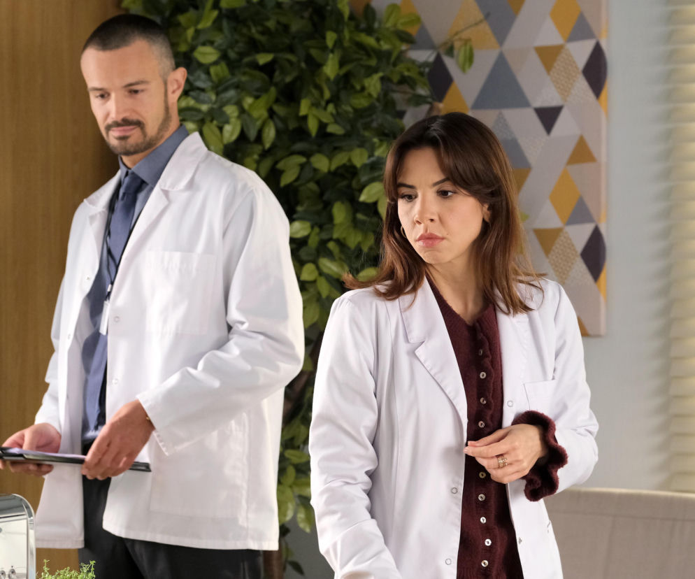 Ilona Janyst jako Aneta i Mikołaj Krawczyk jako Aleksander w białych lekarskich kitlach w gabinecie. Aneta ma zmartwioną minę. Aleksander trzyma teczkę z dokumentami. W tle zielone rośliny i żaluzje. Więcej o ich losach w Super Seriale.
