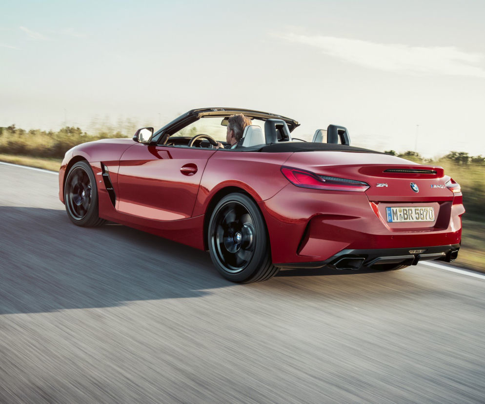 Czerwone BMW Z4 trzeciej generacji z otwartym dachem, dynamicznie poruszające się po drodze, z kierowcą za kierownicą. To symboliczny obraz zmian w motoryzacji, o których możesz przeczytać na naszym portalu. Auto odzwierciedla duszę samochodów tworzonych dla przyjemności kierowcy.
