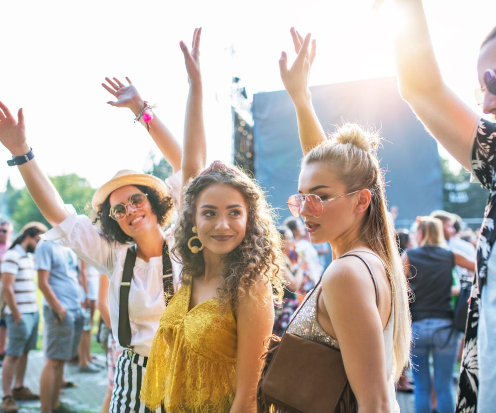 Uśmiechnięci młodzi ludzie bawią się na letnim festiwalu. O pielęgnacji skóry w słońcu przeczytasz na SE.