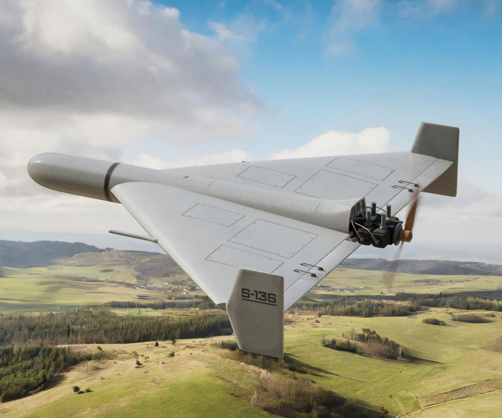 Dron kamikadze typu Shahed leci nad zielonym krajobrazem. O rosyjskich bazach dronów przeczytasz na SE Portal Obronny.