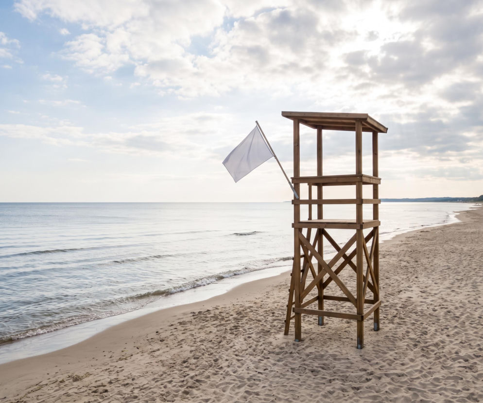 Drewniana wieża ratownicza z białą flagą na pustej plaży w Mrzeżynie. O warunkach kąpieli przeczytasz w SE Szczecin.