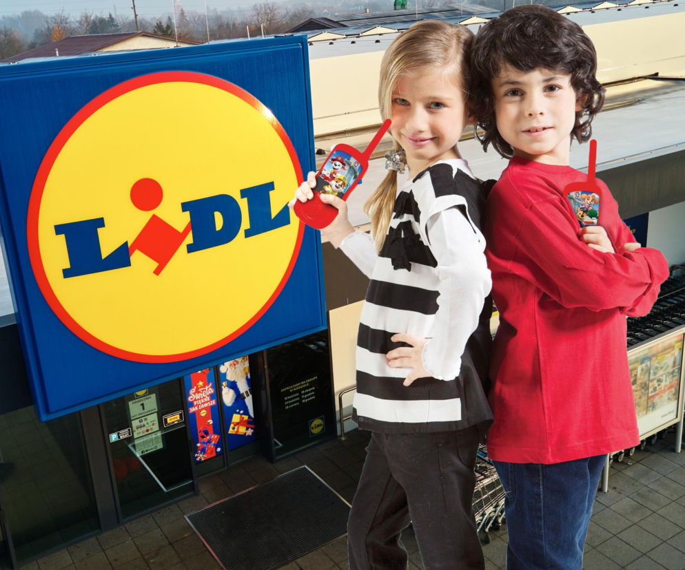 Dziewczynka i chłopiec z krótkofalówkami Lexibook® z motywem Psiego Patrolu na tle wejścia do sklepu Lidl, reklamującego świąteczną ofertę zabawek. O supercenach w Lidlu przeczytasz na Super Biznes.