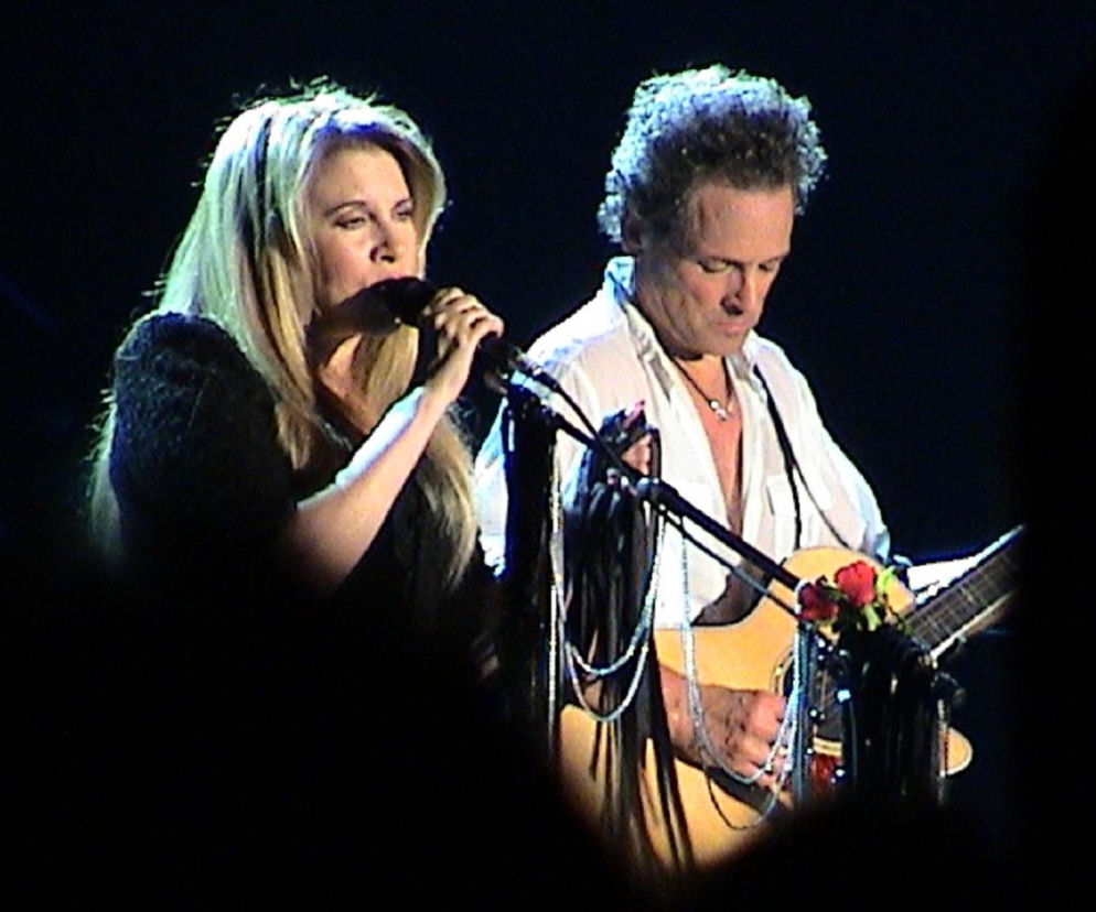 Stevie Nicks śpiewa do mikrofonu, a obok Lindsey Buckingham gra na gitarze. O ikonach Fleetwood Mac czytaj w EskaRock.