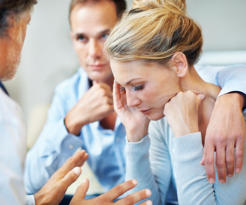 Smutna kobieta u lekarza wspierana przez partnera. O wpływie menopauzy na psychikę przeczytasz na Poradnik Zdrowie.