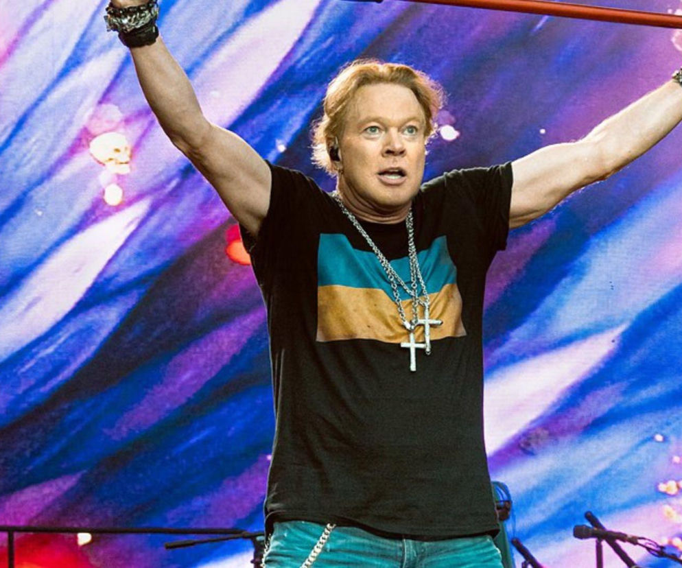 Axl Rose w czarnym t-shircie trzyma mikrofon nad głową. O jego artystycznej drodze przeczytasz na EskaRock.