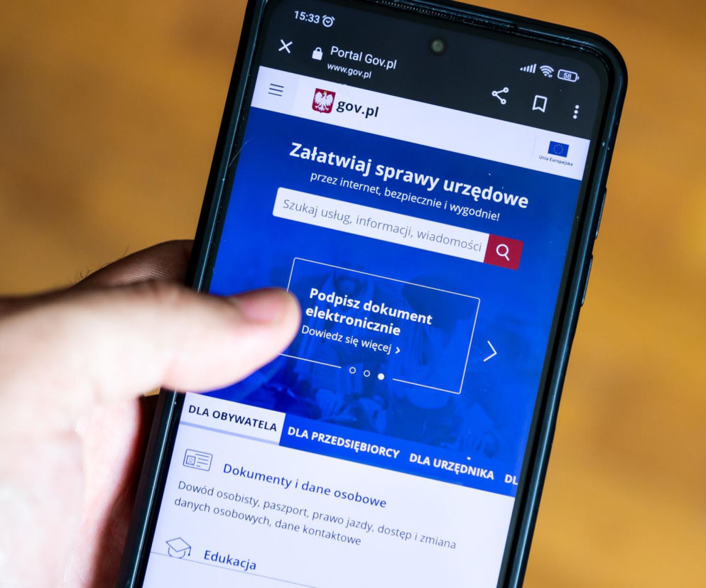 Dłoń trzyma smartfon z otwartym portalem gov.pl. O zastrzeganiu numeru PESEL przeczytasz na SE.