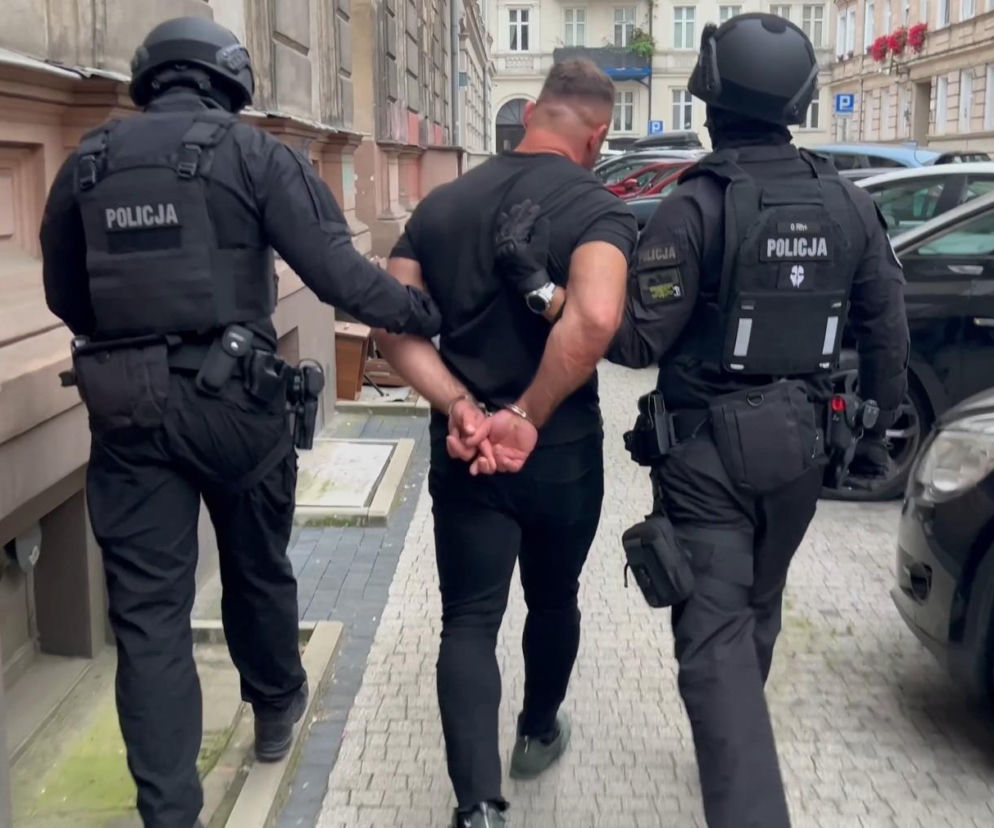 Dwaj uzbrojeni policjanci prowadzą skutego kajdankami mężczyznę. O zatrzymaniu złodzieja złota przeczytasz w Eska Leszno.