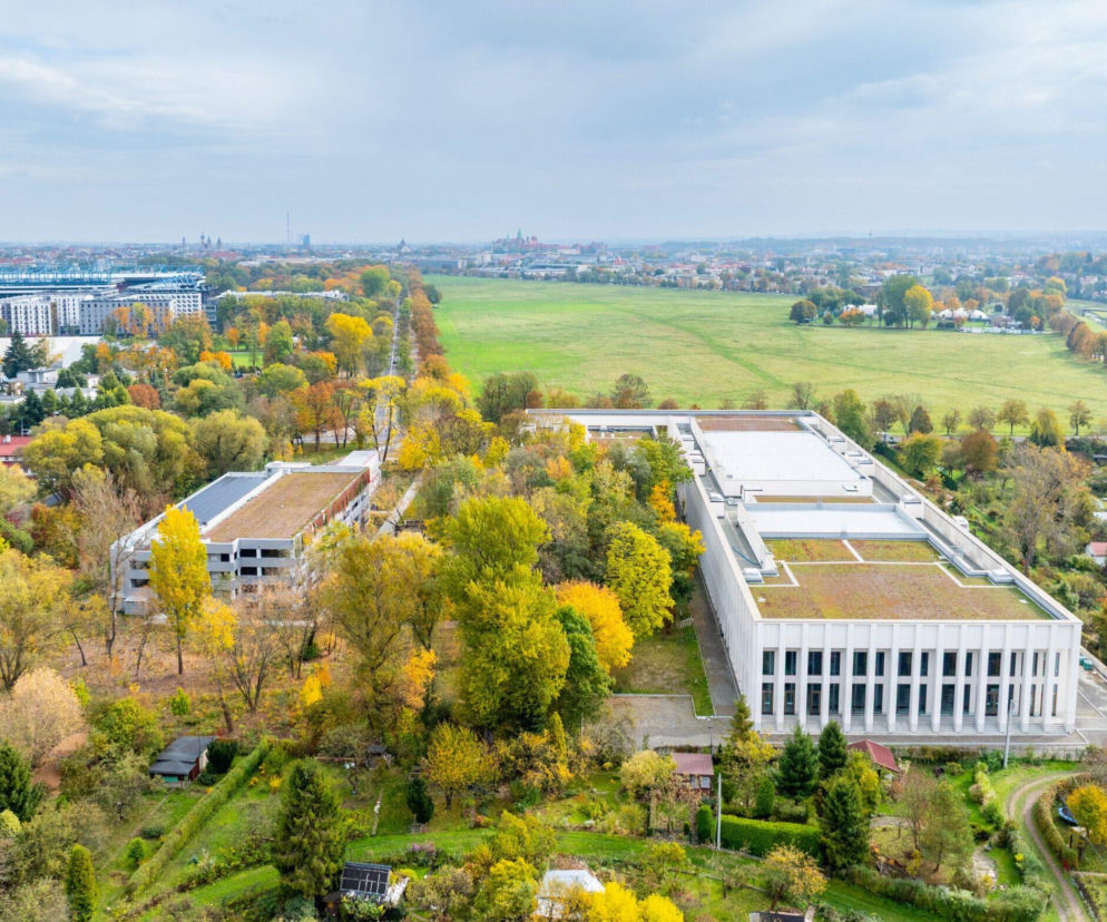 Widok z lotu ptaka na nowoczesny kompleks Krakowskiego Centrum Muzyki z zielonymi dachami, otoczony jesiennym parkiem i rozległymi Błoniami, z panoramą Krakowa w tle. Więcej o architekturze i budownictwie przeczytasz na Architektura Murator Plus.
