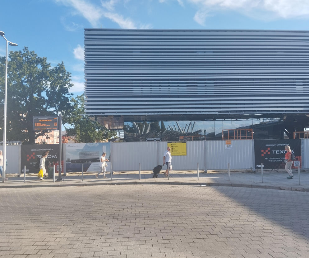 Nowoczesny budynek dworca z pasiastą elewacją. Przed nim płot budowlany i przechodnie. O budowie w Częstochowie czytaj w Architektura.