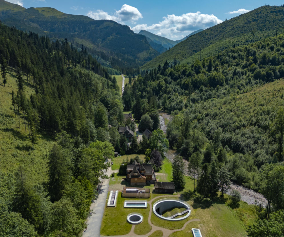 Widok z lotu ptaka na Tatrzańskie Archiwum Planety Ziemia w Dolinie Kościeliskiej. Projekt pracowni Pole Architekci, z drewnianym budynkiem naziemnym i podziemnymi otworami świetlików, dyskretnie wpisany w górski krajobraz. Więcej o tej realizacji na Architektura Murator Plus.