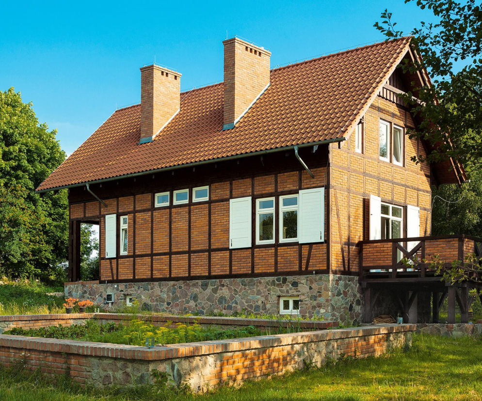 Dom z czerwonym dachem w technologii muru pruskiego na kamiennej podmurówce. O projekcie domu przeczytasz na Muratordom.