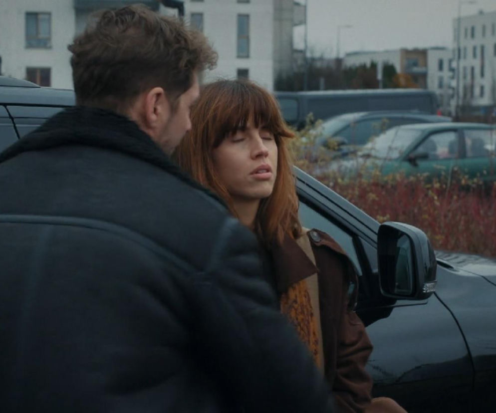 Kama (Michalina Sosna) zasłabła w ramionach Marcina (Mikołaj Roznerski) po rozstaniu, opierając się o czarny samochód. Kobieta ma zamknięte oczy i blada twarz, co widać na zdjęciach dostępnych na portalu Super Seriale. W tle miejski krajobraz z budynkami.