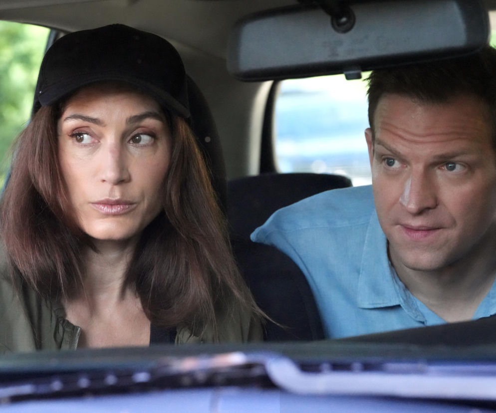 Celina (Orina Krajewska) w czarnej czapce z daszkiem i oliwkowej kurtce oraz Łukasz (Michał Rolnicki) w jasnoniebieskiej koszuli, oboje z zaniepokojonymi minami, siedzą w samochodzie. Spoglądają w lewo, z przodu widać lusterko wsteczne. Aktorzy z serialu Barwy szczęścia, o którym przeczytasz więcej na portalu Super Seriale.