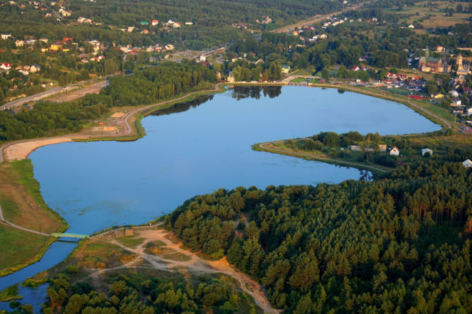 Zalew Mostki z lotu ptaka otoczony gęstym lasem i zabudowaniami. O spokojnych wakacjach przeczytasz na Eska Kielce.