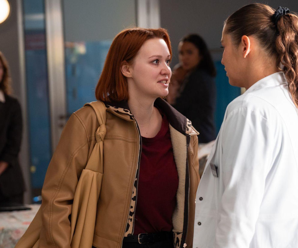 Weronika Walasiewicz (Klemi) w jasnobrązowej kurtce z podszewką w panterkę i Anna Szymańczyk (Iga) w białym lekarskim fartuchu dyskutują w Leśnej Górze, natomiast z tyłu widoczna jest Paulina Napora (kuratorka). O zemście Klemi na Idze przeczytasz na stronie Super Seriale.