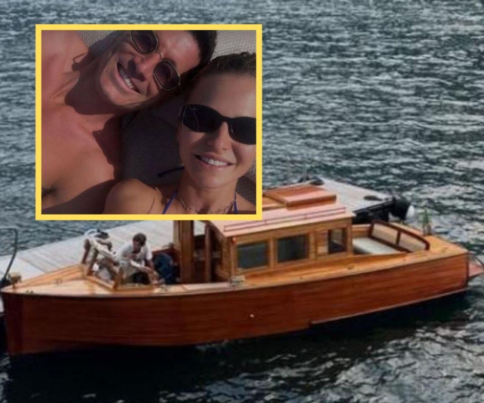 Robert Lewandowski i Anna Lewandowska na wakacjach we Włoszech, uśmiechnięci, w okularach przeciwsłonecznych, widoczni w kadrze, na tle małej drewnianej łodzi zacumowanej przy pomoście na jeziorze. Więcej o ich podróżach przeczytasz na naszym portalu.