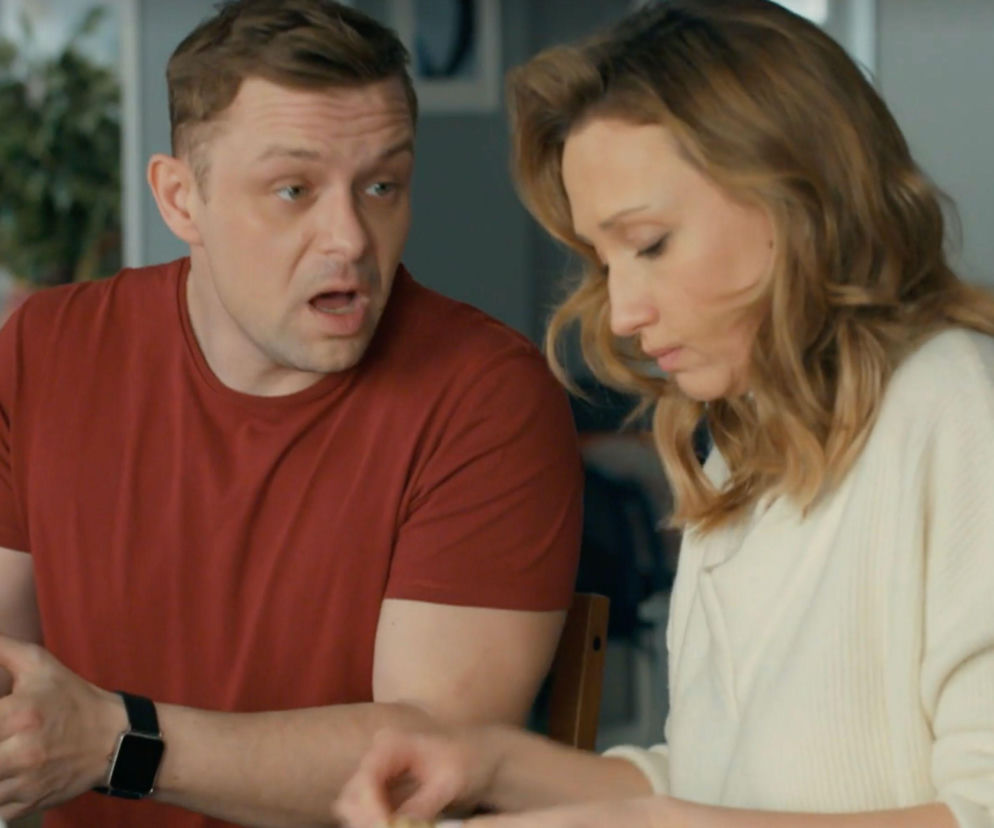 Zaskoczony aktor Marek Kaliszuk w czerwonej koszulce siedzi obok kobiety. Rozwiąż quiz o serialach na Eska.