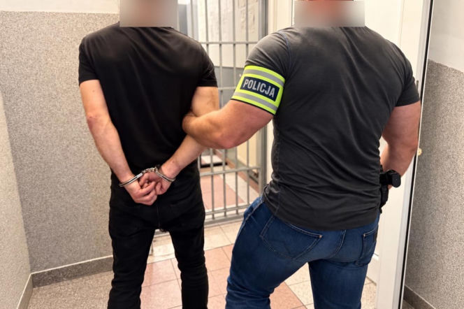 Policjant trzyma skutego kajdankami mężczyznę podejrzanego o porwanie dziecka. O akcji policji czytaj w SE Wrocław.