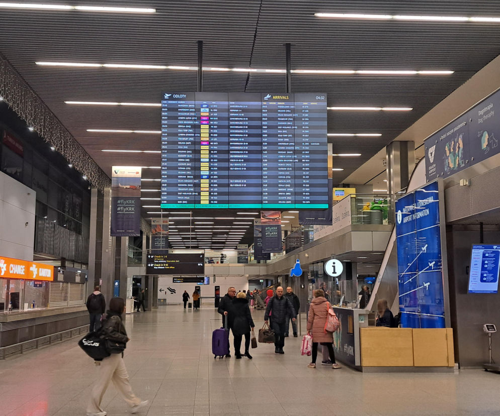 Hala krakowskiego lotniska z pasażerami i tablicą lotów. O cięciach połączeń Wizz Air przeczytasz na SE.