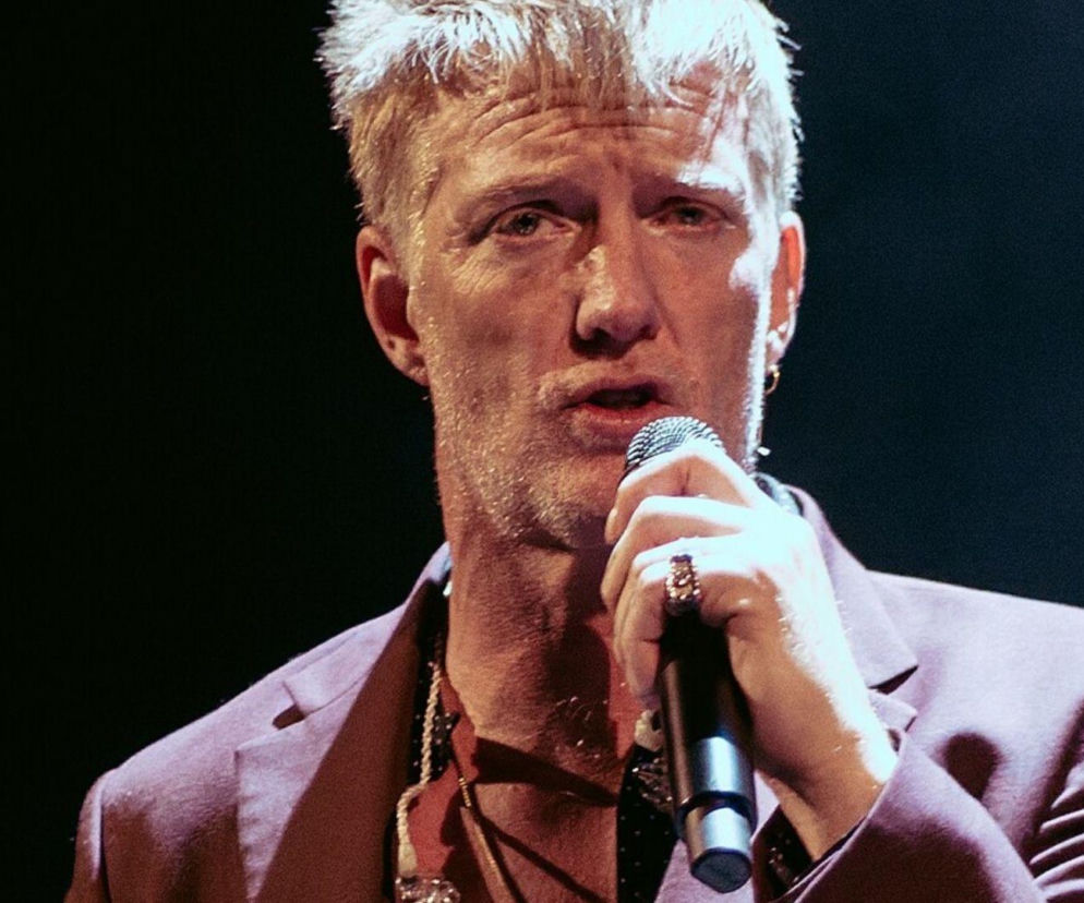 Josh Homme z Queens of the Stone Age trzyma mikrofon podczas występu. O buncie muzyka przeczytasz na EskaRock.