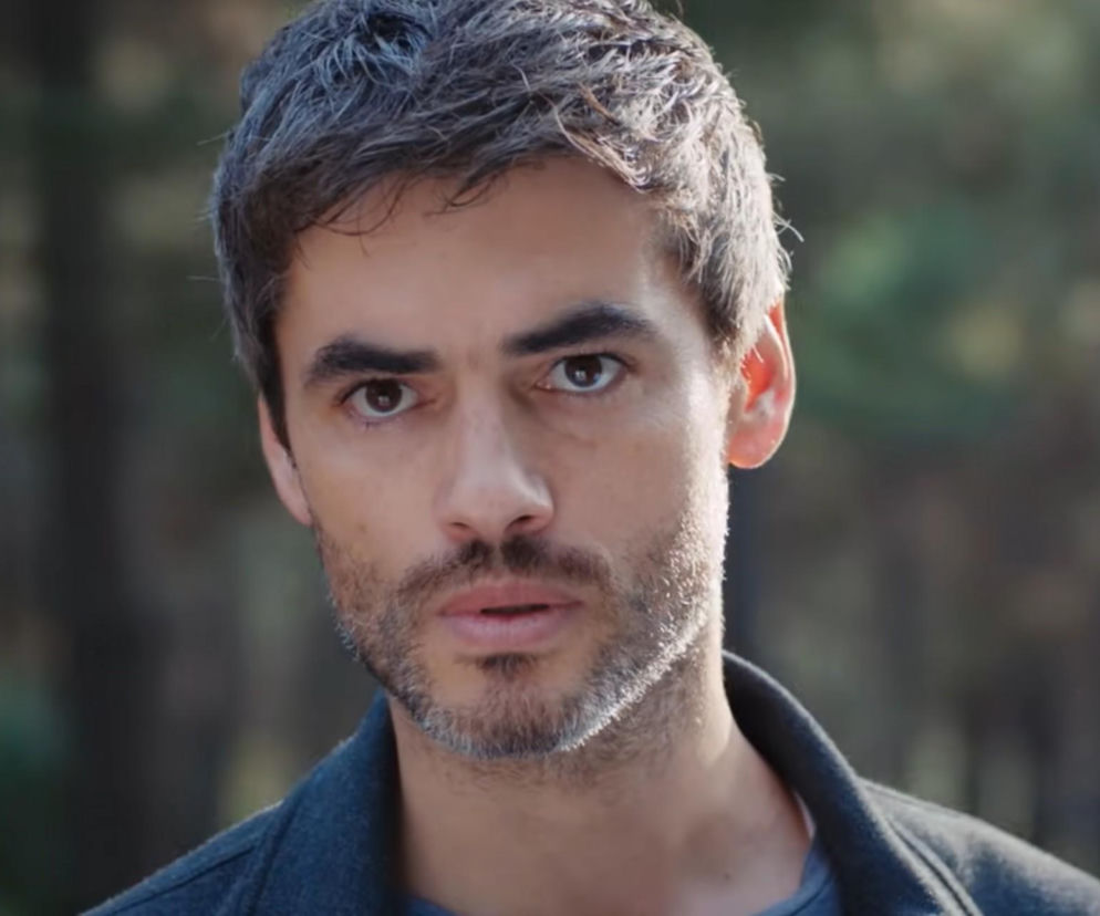 Zbliżenie na twarz mężczyzny z jasnoszarymi włosami i brodą, ubranego w ciemną marynarkę, patrzącego prosto w obiektyw. Zdjęcie ilustruje odcinek 899 tureckiego serialu Dziedzictwo, dostępny na Super Seriale.