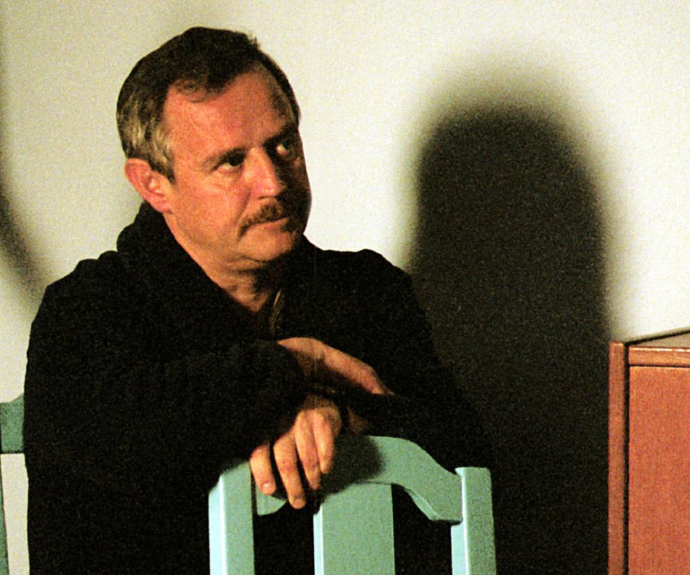 Marek Kondrat jako Adaś Miauczyński opiera się o krzesło. O kultowym filmie Dzień Świra przeczytasz na EskaRock.