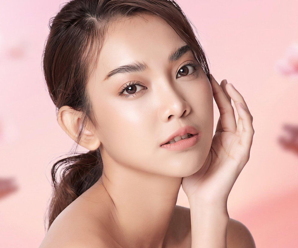 Kobieta o promiennej cerze w naturalnym makijażu dotyka dłonią policzka. O trendach K-beauty przeczytasz na Eska2.