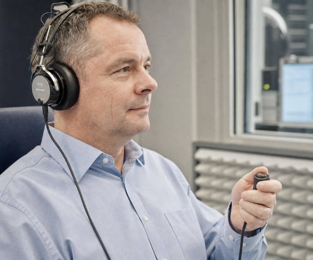 Mężczyzna w słuchawkach audiometrycznych trzyma przycisk do sygnalizacji dźwięku. O badaniu słuchu czytaj na Poradnik Zdrowie.