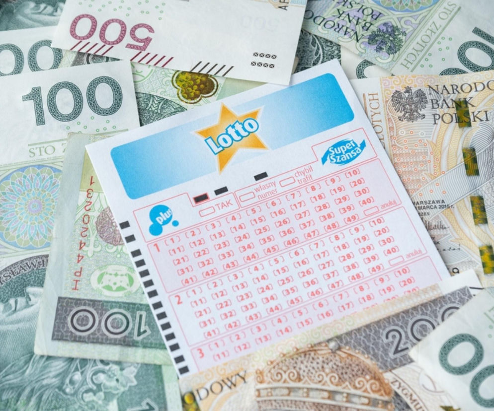Blankiet kuponu Lotto z logo Plus i Super Szansa leży na rozrzuconych banknotach polskich złotych (100, 200, 500 zł), symbolizując szansę na wysoką wygraną w kumulacji. O prognozach i wynikach losowań przeczytasz na Super Biznes.