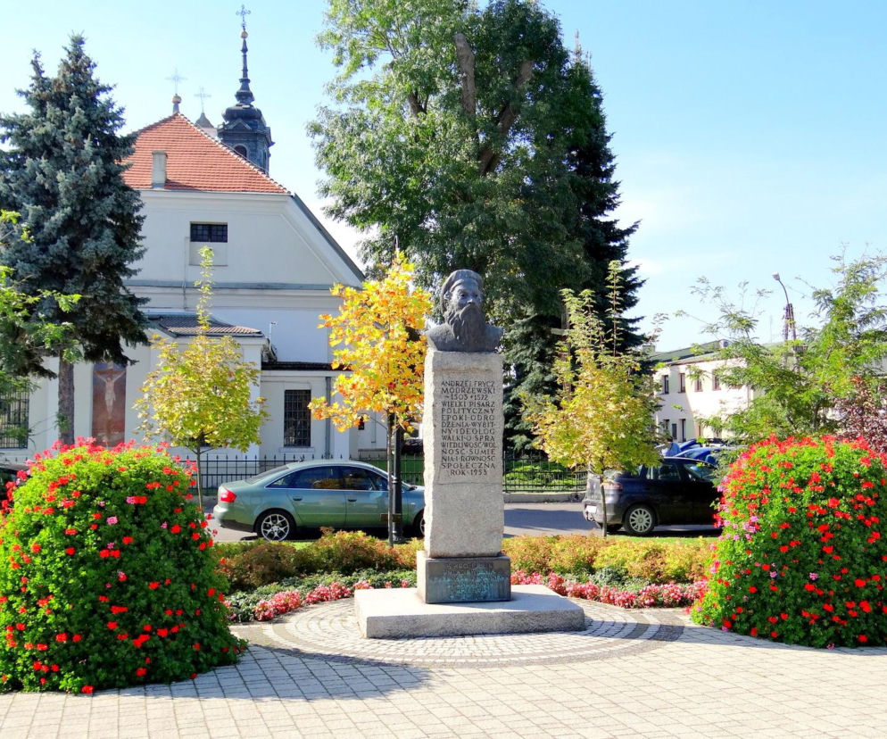 Pomnik Andrzeja Frycza Modrzewskiego w Wolborzu na tle zabytkowej kolegiaty. O historii miasta czytaj w Eska Łódź.