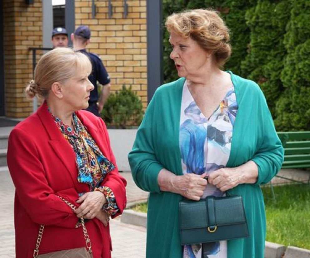 Józefina (Elżbieta Jarosik) i Walczewska (Małgorzata Puzio) z serialu Barwy szczęścia rozmawiają na zewnątrz, Walczewska ubrana w czerwoną marynarkę, a Józefina w zielony kardigan, trzymając torebkę. Możesz dowiedzieć się więcej o ich losach na stronie Super Seriale.