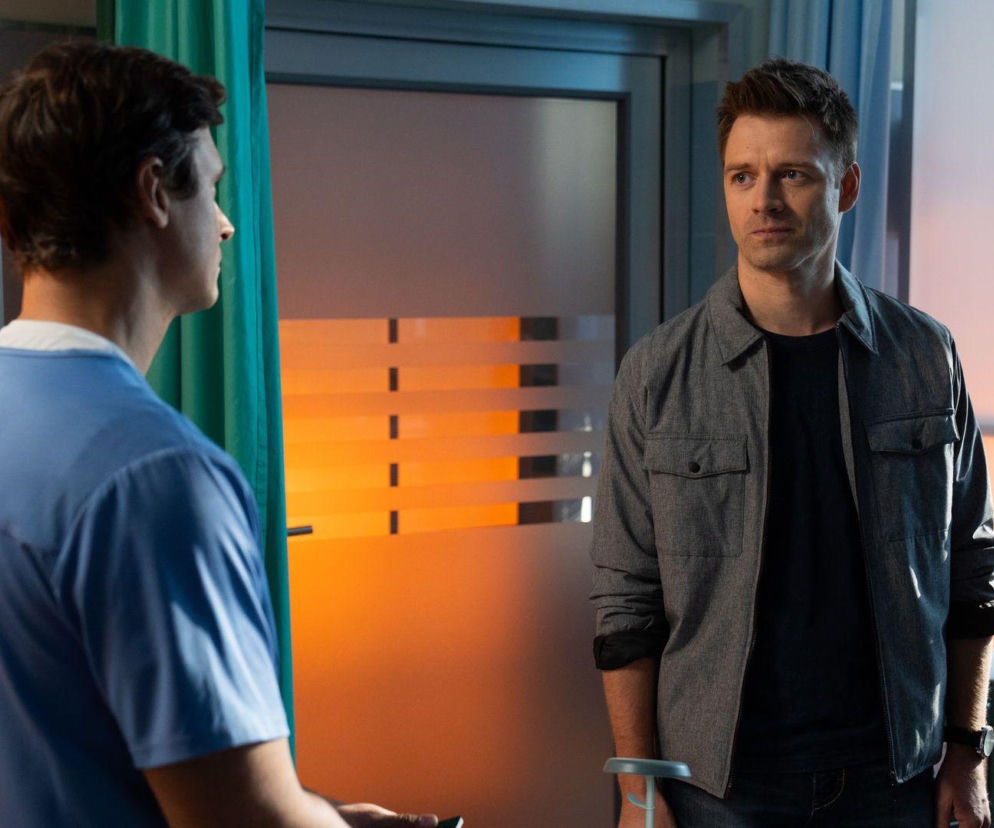 Krzysztof Radwan w niebieskim stroju medycznym i Mario w szarej koszuli stoją naprzeciwko siebie, rozmawiając w pomieszczeniu szpitalnym. Scena z odcinka serialu Na dobre i na złe gdzie Mario dziękuje Radwanowi. Więcej informacji znajdziesz na Super Seriale.