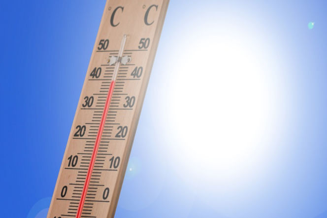 Drewniany termometr wskazuje wysoką temperaturę powyżej 40 stopni Celsjusza, na tle jasnego błękitnego nieba z oślepiającym słońcem, symbolizującym falę upałów w Neapolu, o której przeczytasz więcej na naszym portalu.
