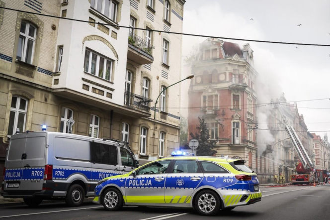 Radiowozy na ulicy przy palącej się kamienicy. Strażacy gaszą ogień z drabiny. O pożarze w Katowicach czytaj na Eska Śląskie.
