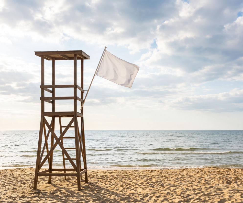 Drewniana wieża ratownicza z białą flagą na pustej plaży w Rewalu. O warunkach nad morzem przeczytasz na SE Szczecin.
