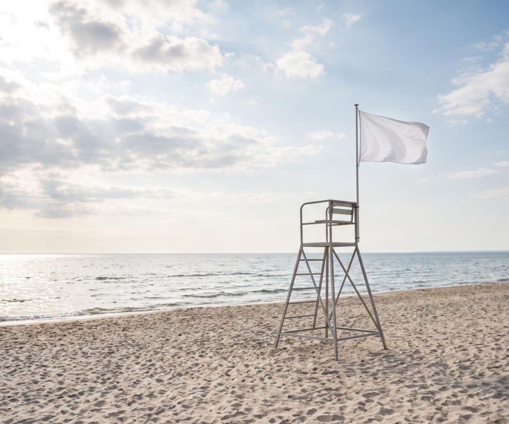 Biała flaga na wieży ratowniczej na pustej plaży w Mielnie. O warunkach nad Bałtykiem przeczytasz na SE Szczecin.