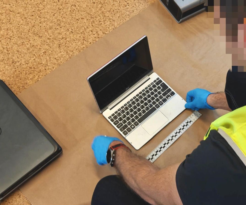 Ręce policjanta w rękawiczkach zabezpieczają laptopa podczas śledztwa. O zatrzymaniu 34-latka przeczytasz na SE.