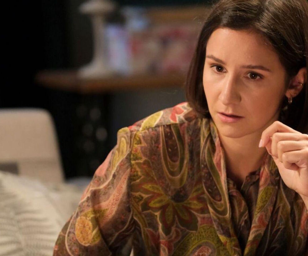 Młoda kobieta, Agnes (Amanda Mincewicz), o krótkich, ciemnych włosach i zamyślonym wyrazie twarzy, ubrana w kwiecistą bluzkę. Na jej nadgarstku widać delikatną bransoletkę. Scena z serialu M jak miłość, o której możesz przeczytać na portalu Super Seriale.