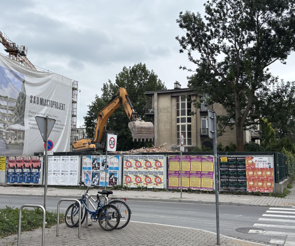 Koparka na tle krakowskiej willi i ogrodzenia z plakatami. O wyburzeniu zabytku przy Focha przeczytasz na Architektura.